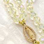 Close-up of a crystal rosary bracelet featuring sparkling yellow beads, gold-tone cross pendant, and Marian medal detail.