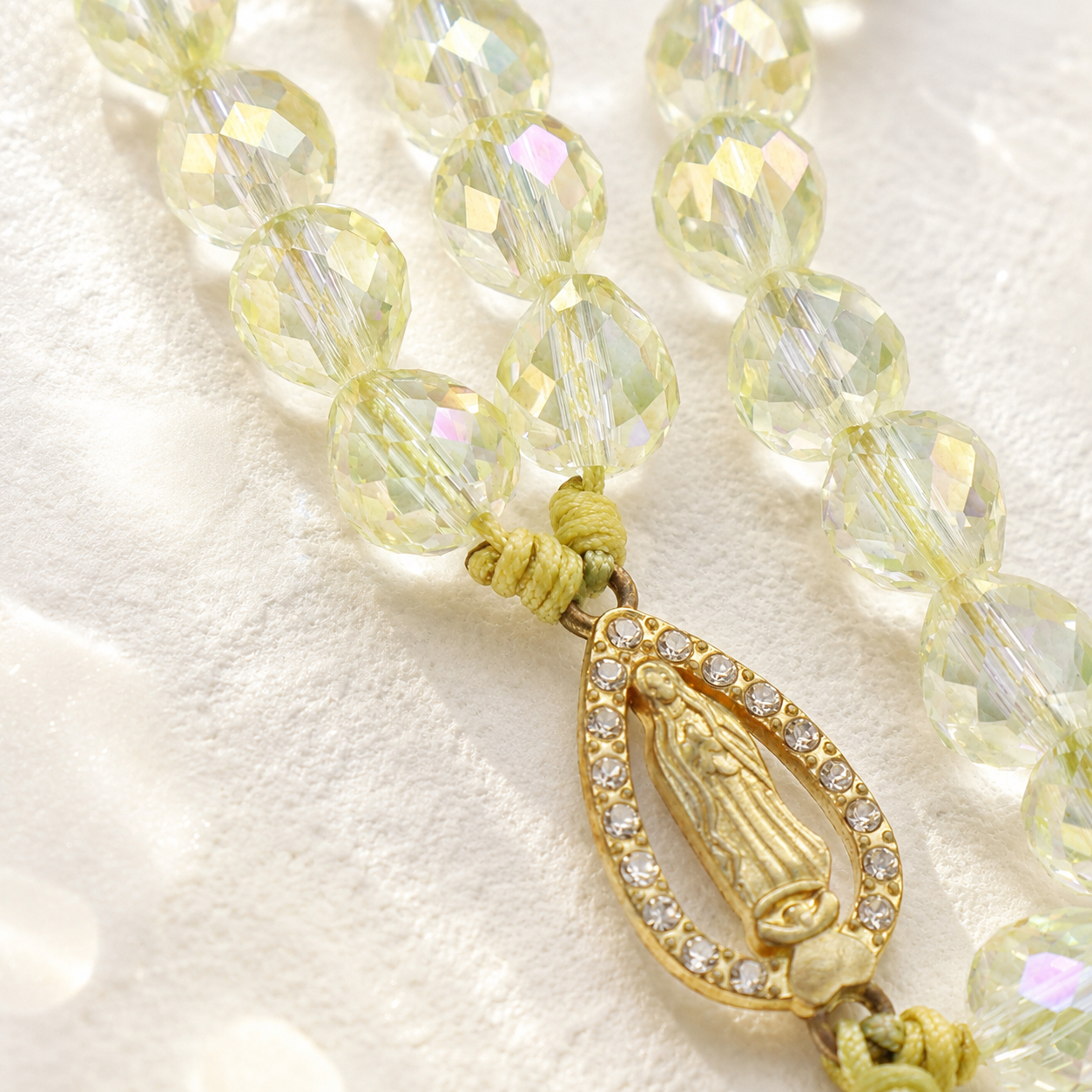 Close-up of a crystal rosary bracelet featuring sparkling yellow beads, gold-tone cross pendant, and Marian medal detail.