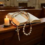 Catholic rosary necklace with crucifix and prayer beads on an open Bible beside a candle in church