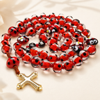 Red ladybug Catholic rosary featuring transparent glass beads, handmade details, and a gold cross pendant for personal prayer.