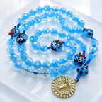Blue glass bead Catholic rosary with playful ladybug charms and a gold religious centerpiece, a unique prayer gift for everyday devotion.