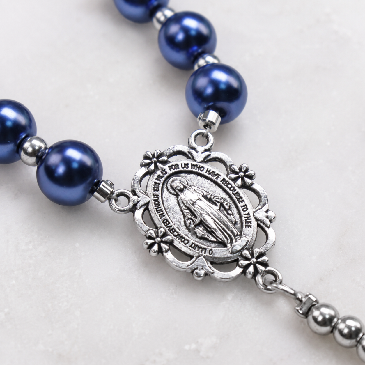 Close-up of deep blue pearl rosary beads with silver Our Lady medal, St. Benedict style details, and handcrafted Catholic prayer design.