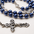 Silver crucifix pendant on a blue pearl Catholic rosary, showing detailed Christian symbols and traditional prayer bead craftsmanship.