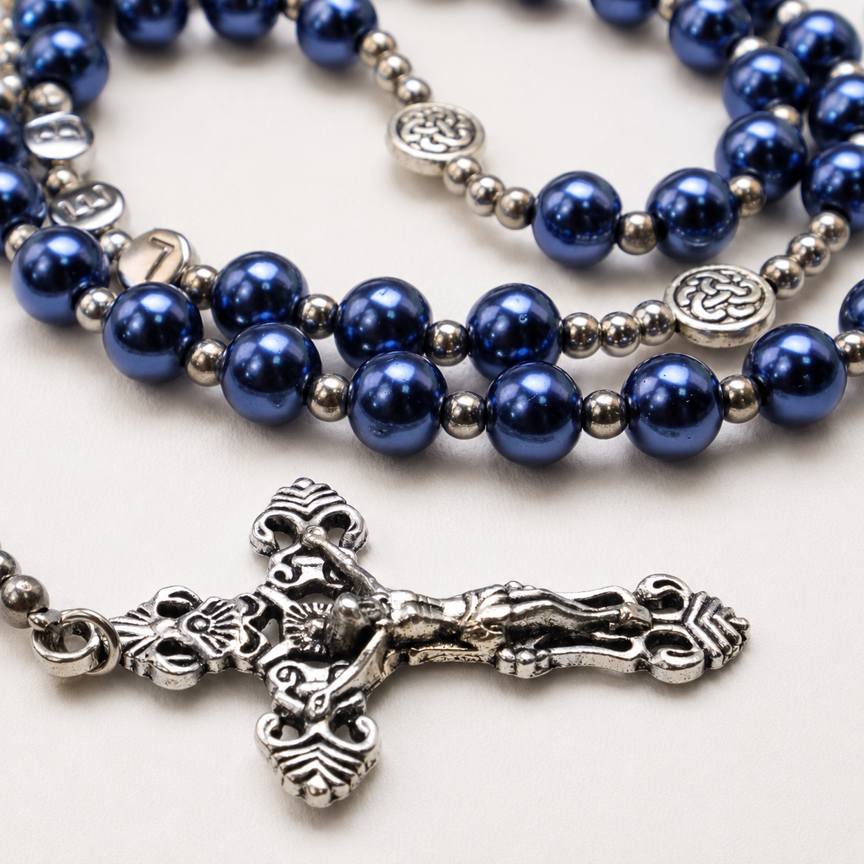 Silver crucifix pendant on a blue pearl Catholic rosary, showing detailed Christian symbols and traditional prayer bead craftsmanship.