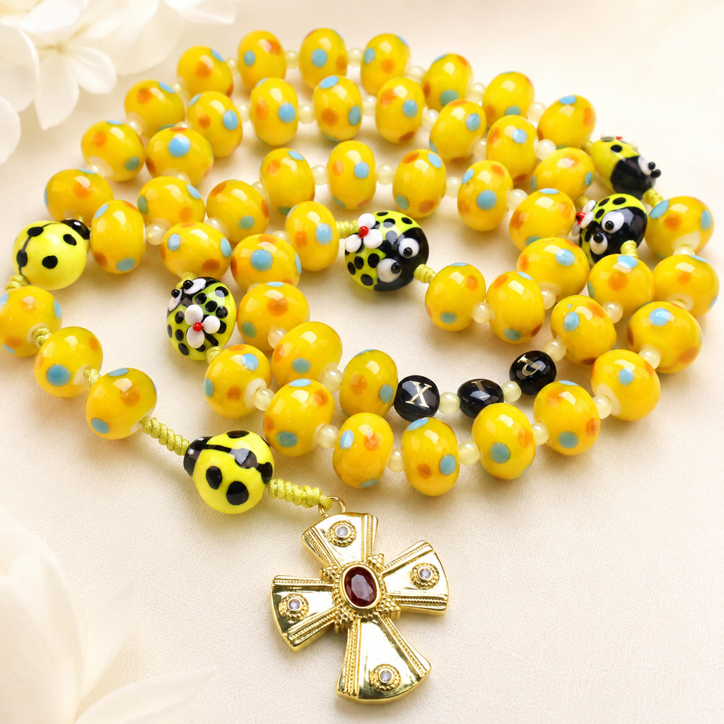Yellow Catholic rosary with handmade glass beads and ladybug details, featuring a gold crucifix for joyful prayer and faith inspiration.
