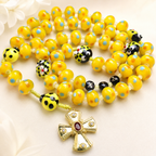 Yellow Catholic rosary with handmade glass beads and ladybug details, featuring a gold crucifix for joyful prayer and faith inspiration.