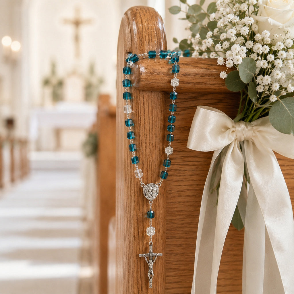 Blue wedding rosary hanging on a church pew with white flowers and ribbon, creating a beautiful Catholic bridal ceremony decoration and meaningful wedding blessing symbol.