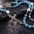 Close-up of a silver crucifix pendant on a handmade blue Catholic rosary with soft blue and white beads.