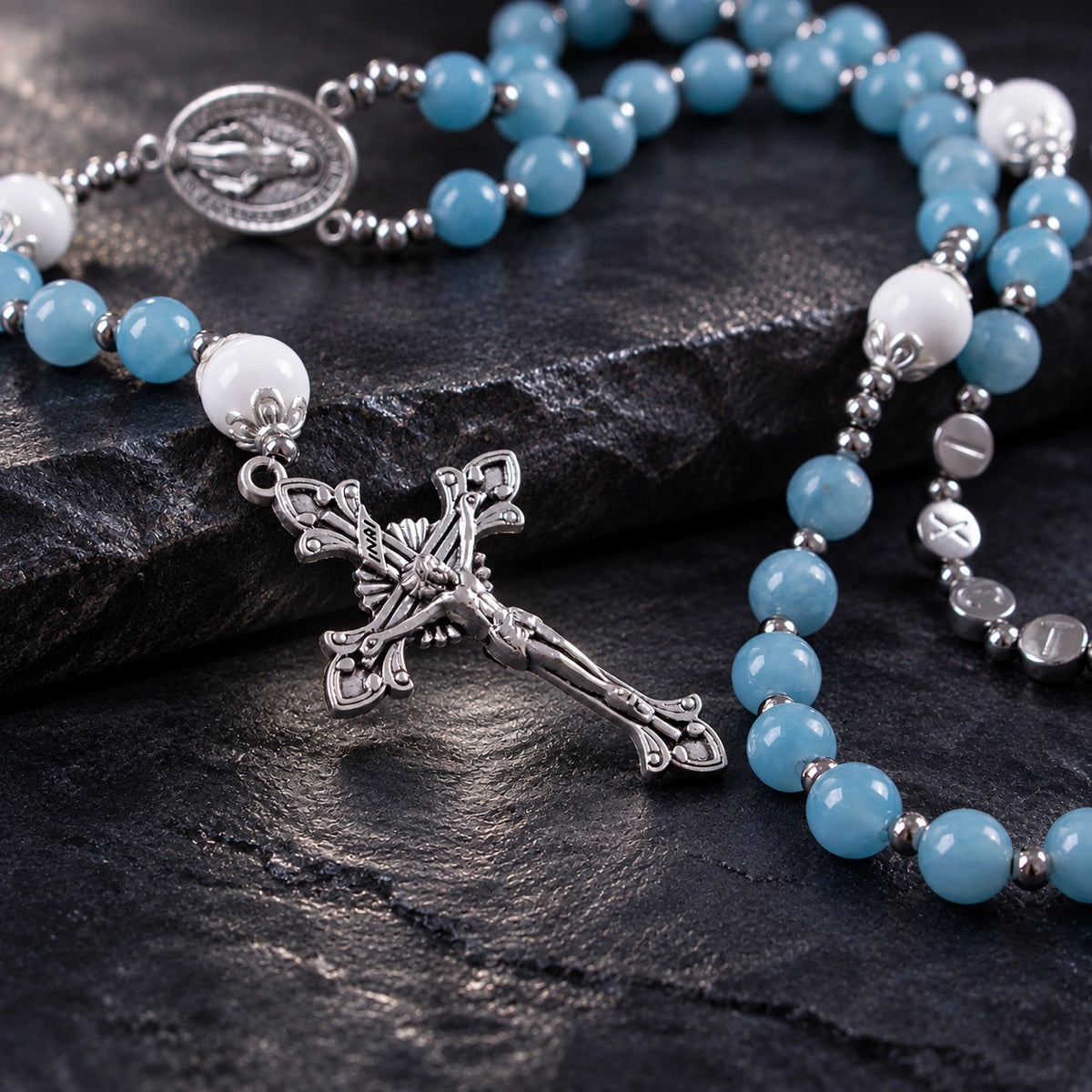 Close-up of a silver crucifix pendant on a handmade blue Catholic rosary with soft blue and white beads.
