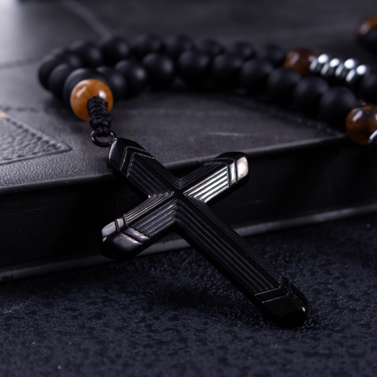 Men’s Catholic rosary featuring matte black beads, tiger-eye accent beads, and dark metal spacer details.