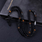 Close-up of a black crucifix pendant on a handmade men’s Catholic rosary with matte black prayer beads.