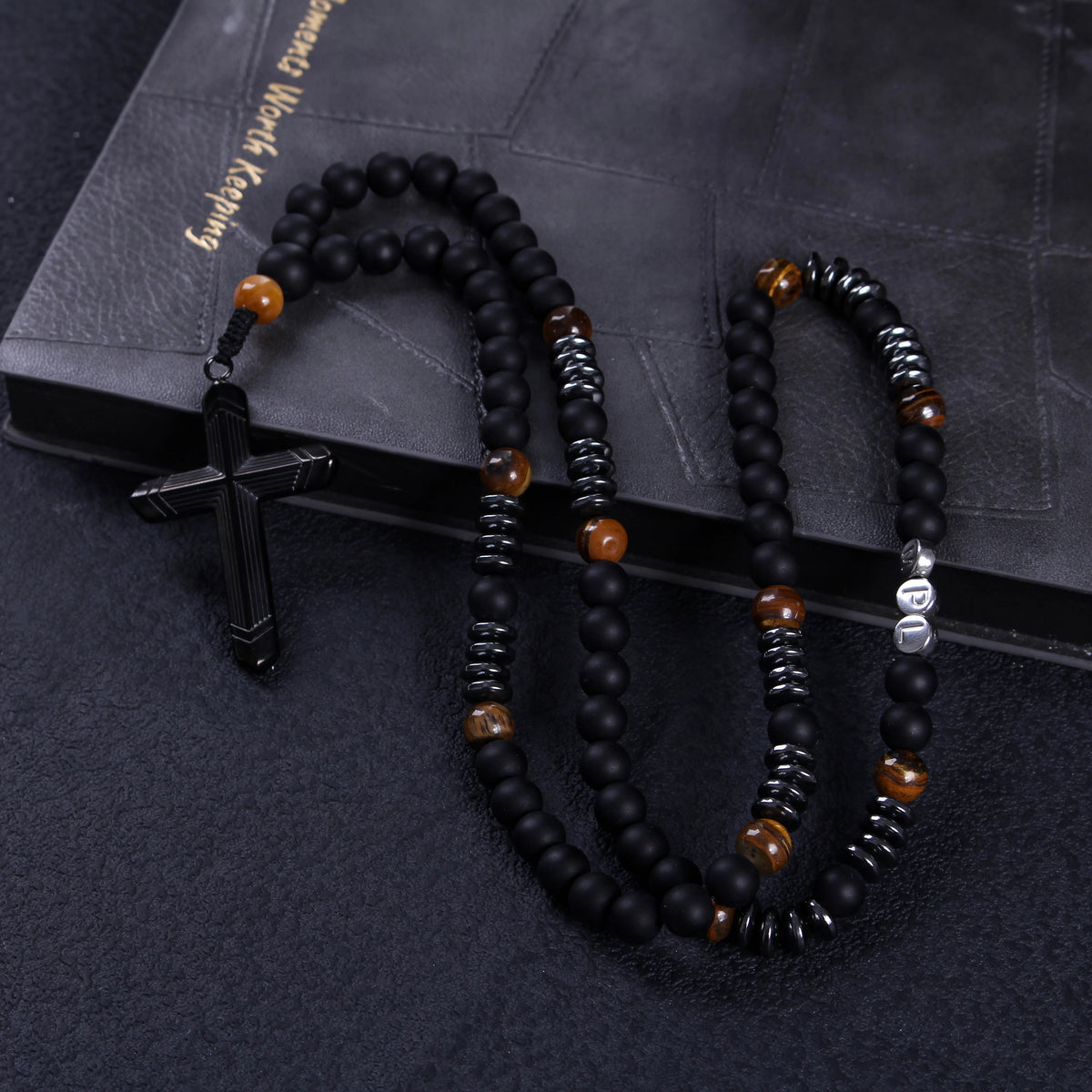 Close-up of a black crucifix pendant on a handmade men’s Catholic rosary with matte black prayer beads.