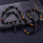 Stone Guardian Rosary featuring black prayer beads, earthy tiger-eye tones, green stone-style accents, and a bold black cross pendant.