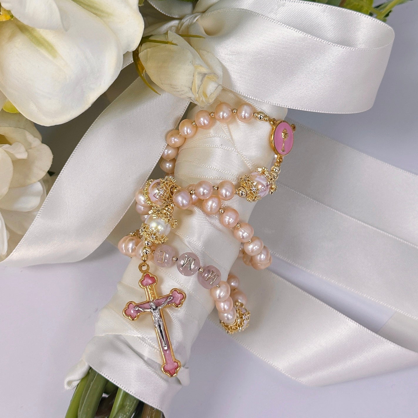 Personalized pink pearl Catholic wedding rosary for bride with gold crucifix, chalice medal, and initial beads styled on a bridal bouquet