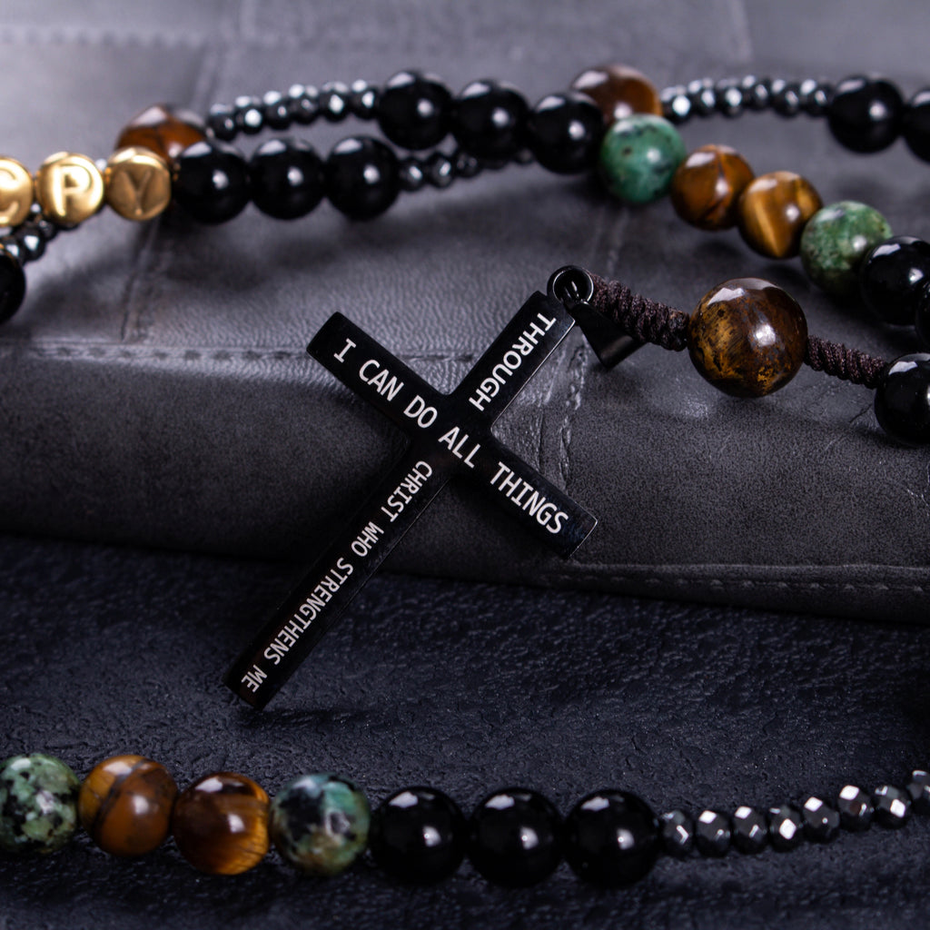 Close-up of a black crucifix pendant on a handmade men’s Catholic rosary with dark beads and natural stone accents.