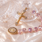 Pink crystal Catholic charm with gold crucifix, Marian medal, and soft pearl accents, designed as a meaningful faith accessory.