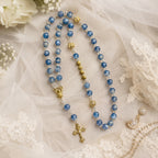 Blue Catholic bridal rosary displayed with wedding rings and ivory lace, designed as a meaningful Something Blue wedding keepsake