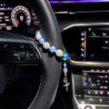 Blue Catholic car rosary displayed on a steering wheel with soft blue and white beads, personalized initial charm, Miraculous Medal, and silver crucifix