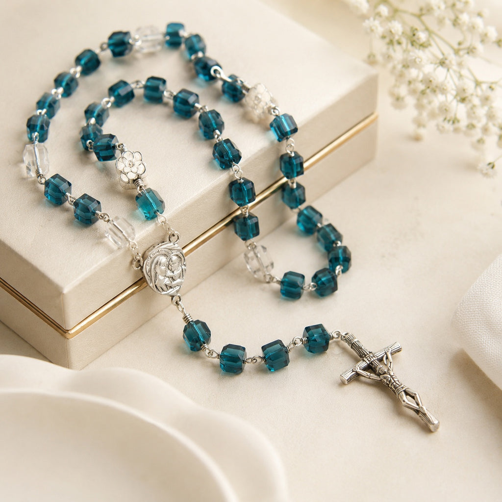 Blue Catholic rosary with crystal-style beads, Virgin Mary medal, and silver crucifix displayed on an elegant cream gift box