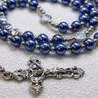 Close-up of a blue Catholic rosary with pearl-like beads and silver crucifix on a textured background, showing detailed prayer beads and faith jewelry design.