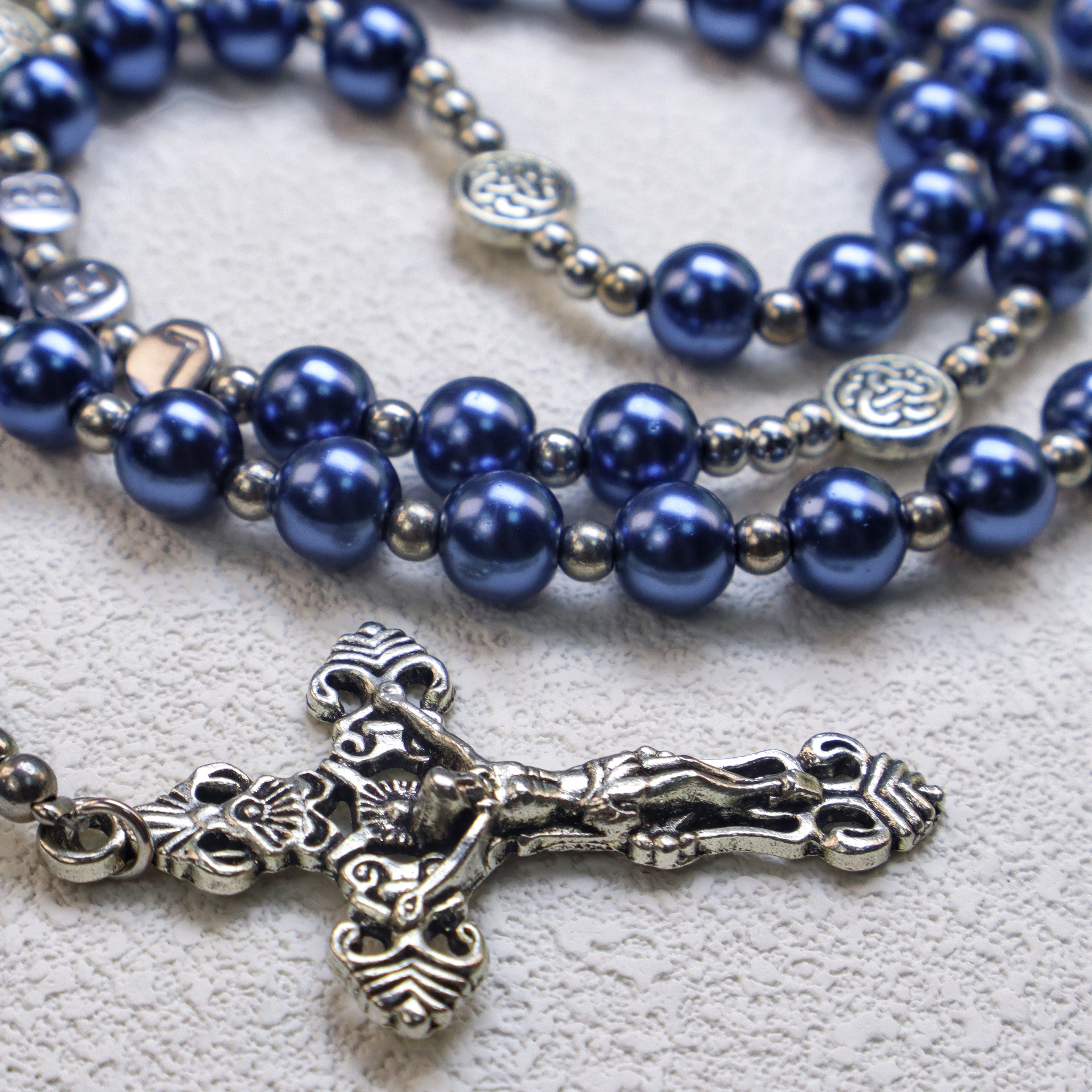 Close-up of a blue Catholic rosary with pearl-like beads and silver crucifix on a textured background, showing detailed prayer beads and faith jewelry design.