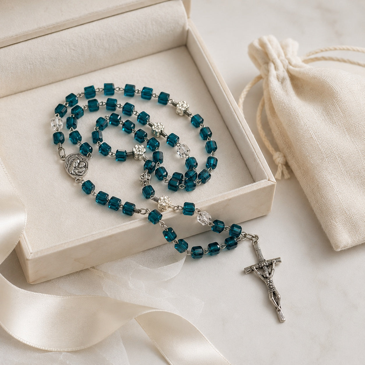 Blue Catholic prayer beads with clear accent beads and silver-tone crucifix, photographed on a soft cream devotional gift setting