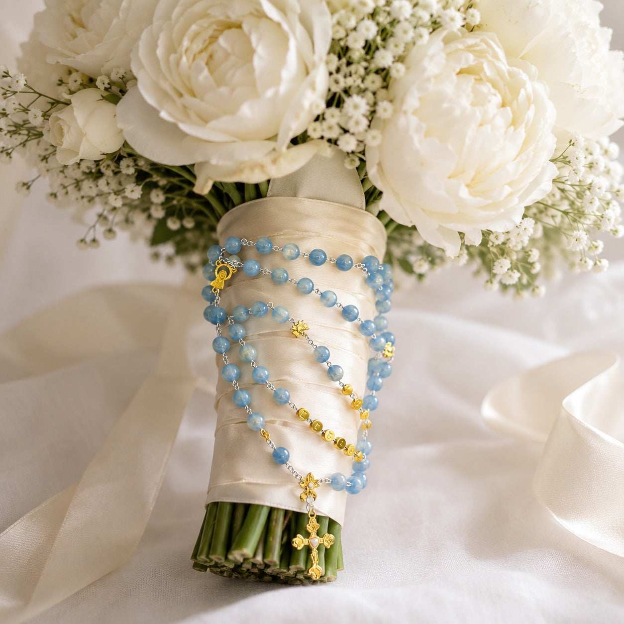 Bride bouquet wrapped with a blue Catholic wedding rosary featuring gold-tone details, devotional medal, and delicate prayer beads