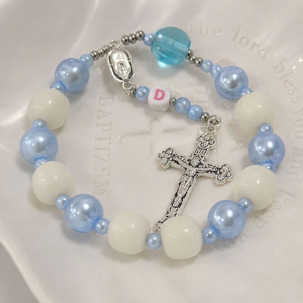 Blue and white Catholic car prayer beads with custom initial charm and silver crucifix, shown as a faith accessory for daily driving