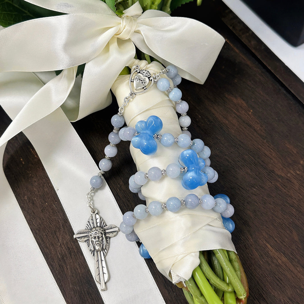 Something Blue Catholic wedding rosary for bride with soft blue beads, floral accents, silver crucifix, and heart medal styled on a bridal bouquet
