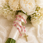 Soft pink bridal rosary wrapped around a white wedding bouquet, designed as a meaningful Catholic wedding keepsake for the bride