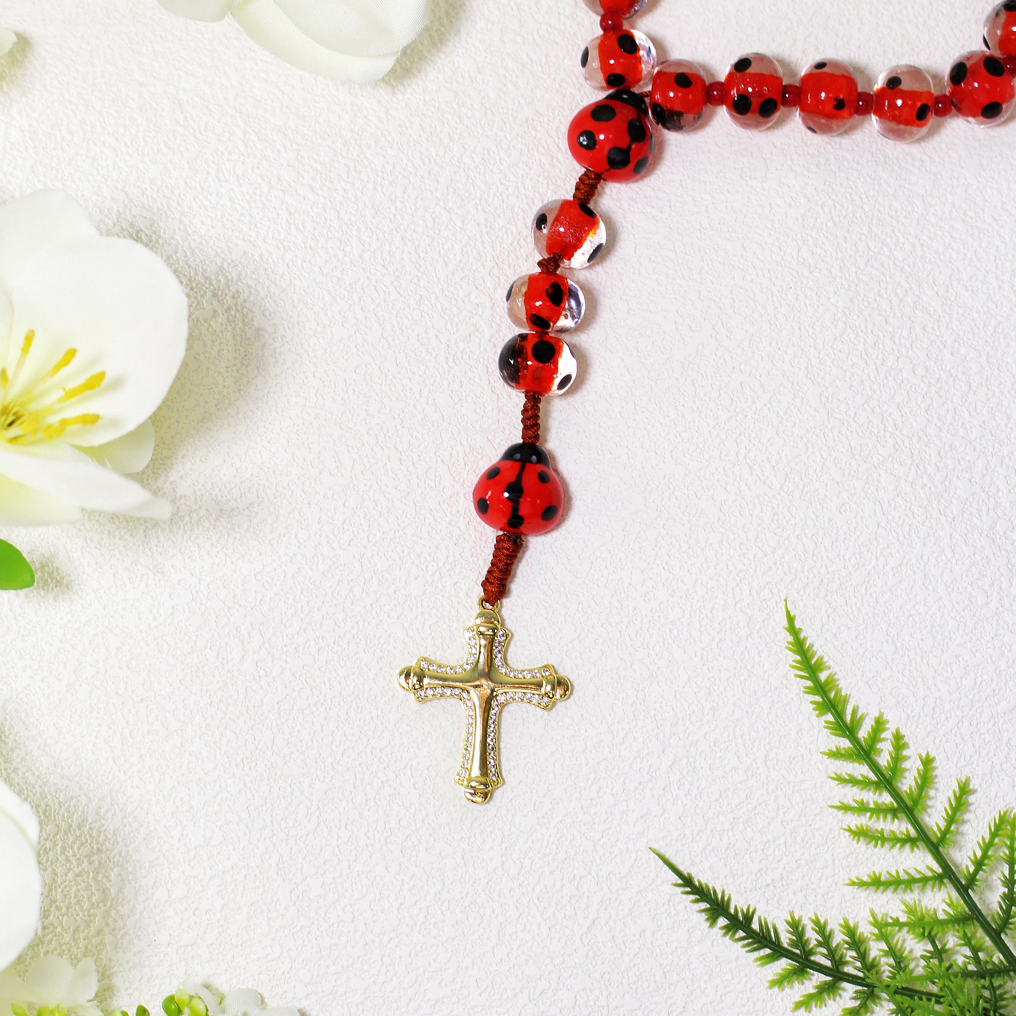 Close-up of a ladybug rosary featuring red and black ladybug beads, natural stone beads, and a Christian cross pendant