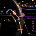 Pink crystal Catholic car rosary wrapped around a steering wheel with personalized initial bead and gold crucifix