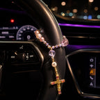 Pink crystal Catholic car rosary wrapped around a steering wheel with personalized initial bead and gold crucifix