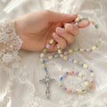 Pastel Catholic rosary displayed with white roses and lace, featuring multicolor beads and silver crucifix for a bridal wedding gift