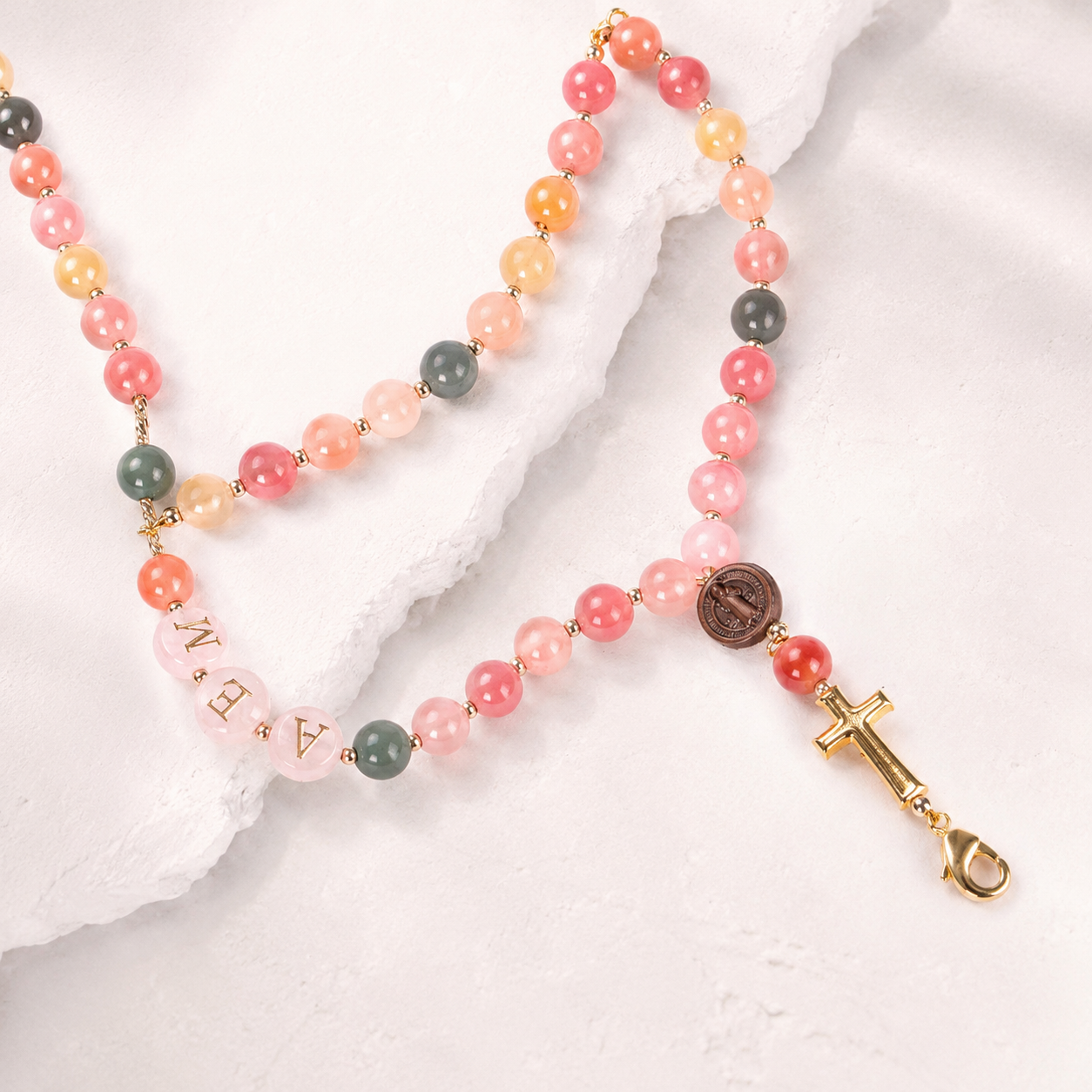 Close-up of a handmade personalized rosary bracelet with pastel beads, gold spacers, custom initials, and Catholic religious charms.