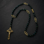 Close-up view of handmade Catholic rosary featuring green gemstone beads, gold tone links, and traditional St. Benedict crucifix