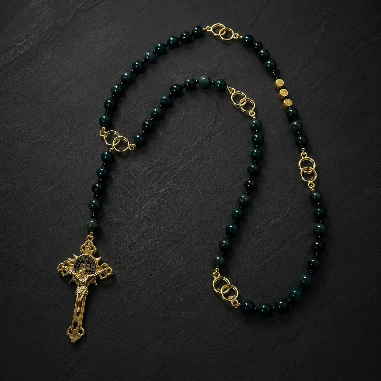 Close-up view of handmade Catholic rosary featuring green gemstone beads, gold tone links, and traditional St. Benedict crucifix