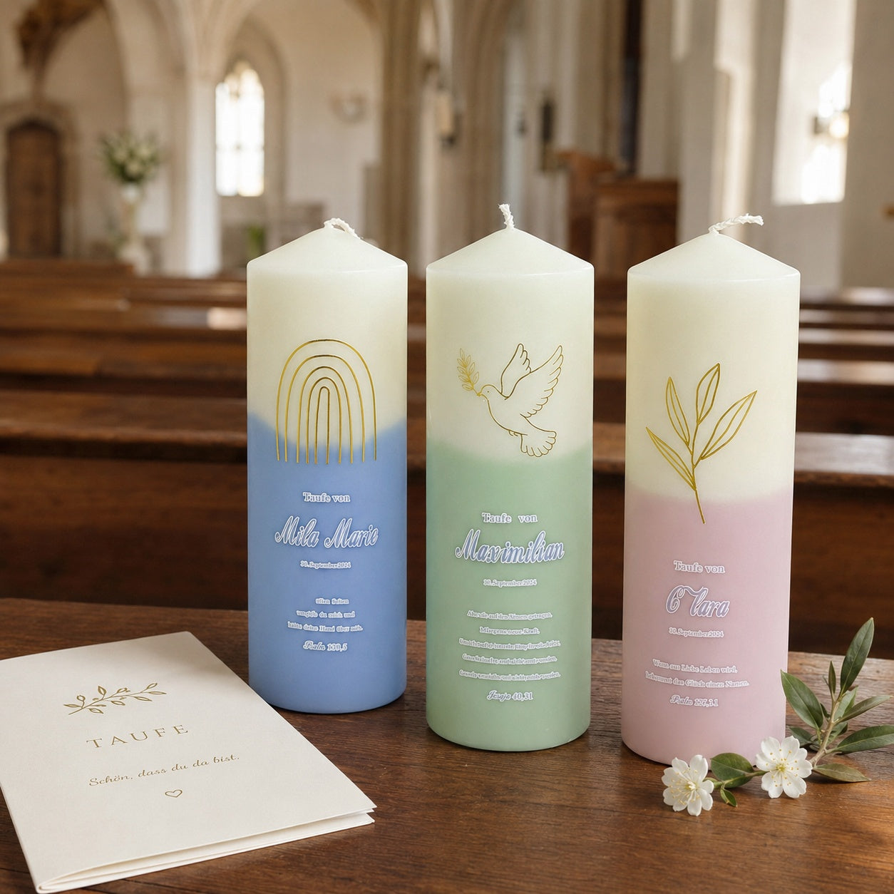 Personalized baptism candle with soft pastel pink and green gradient, gold olive branch and dove artwork, styled with baby christening clothes, baptism card, and delicate white flowers.