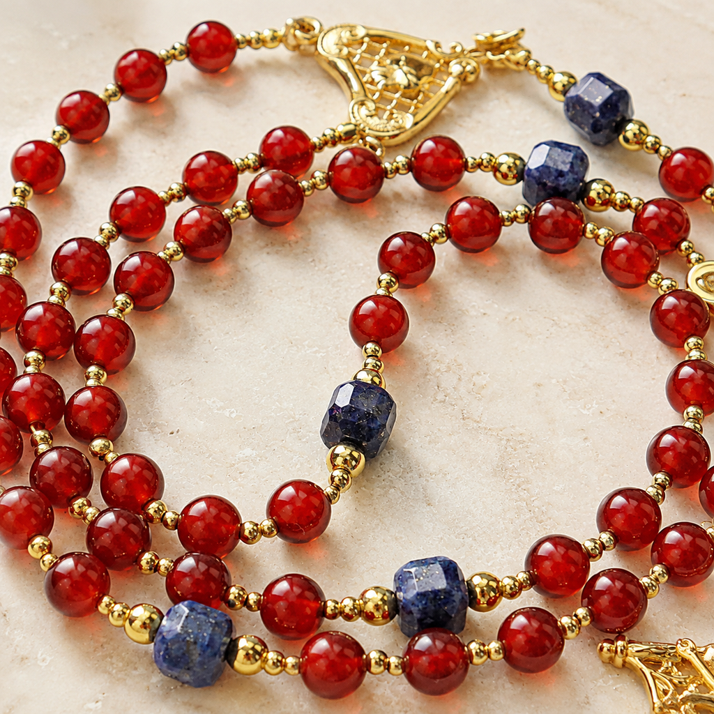 Detailed view of red prayer beads with blue gemstone accents and gold spacers on a handmade Catholic rosary.
