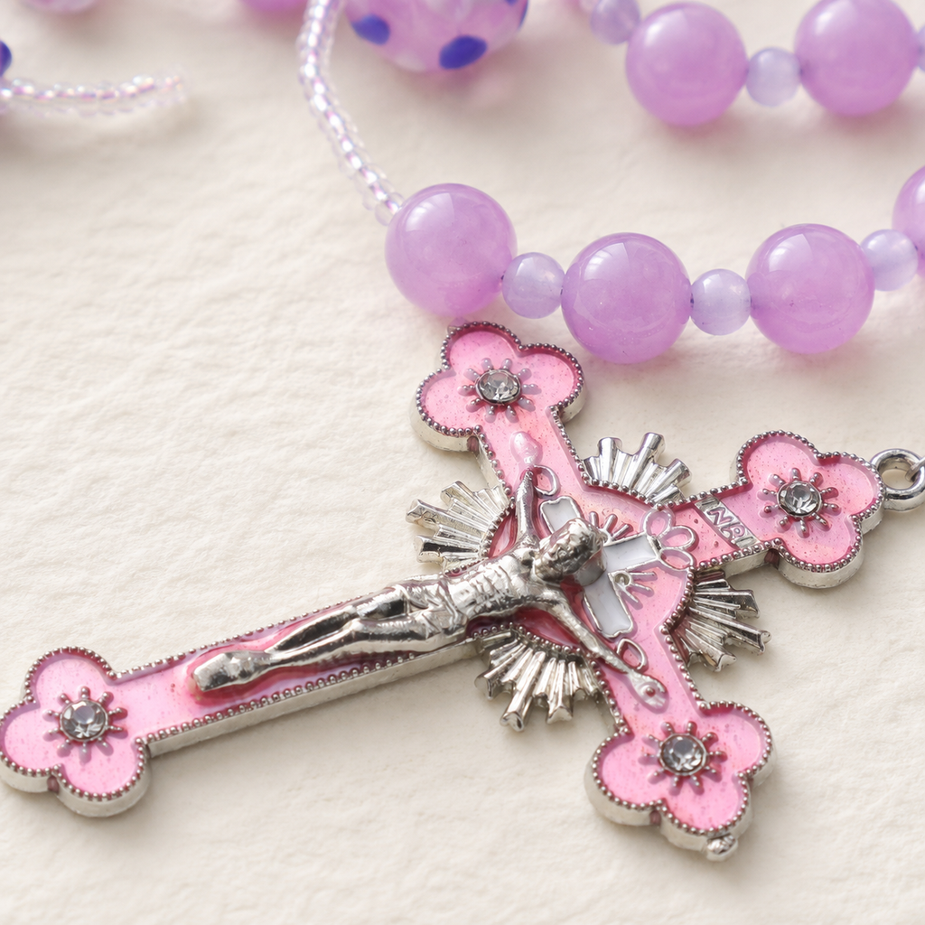 Pink crucifix pendant on a lavender Catholic rosary with floral bead accents and feminine faith design.