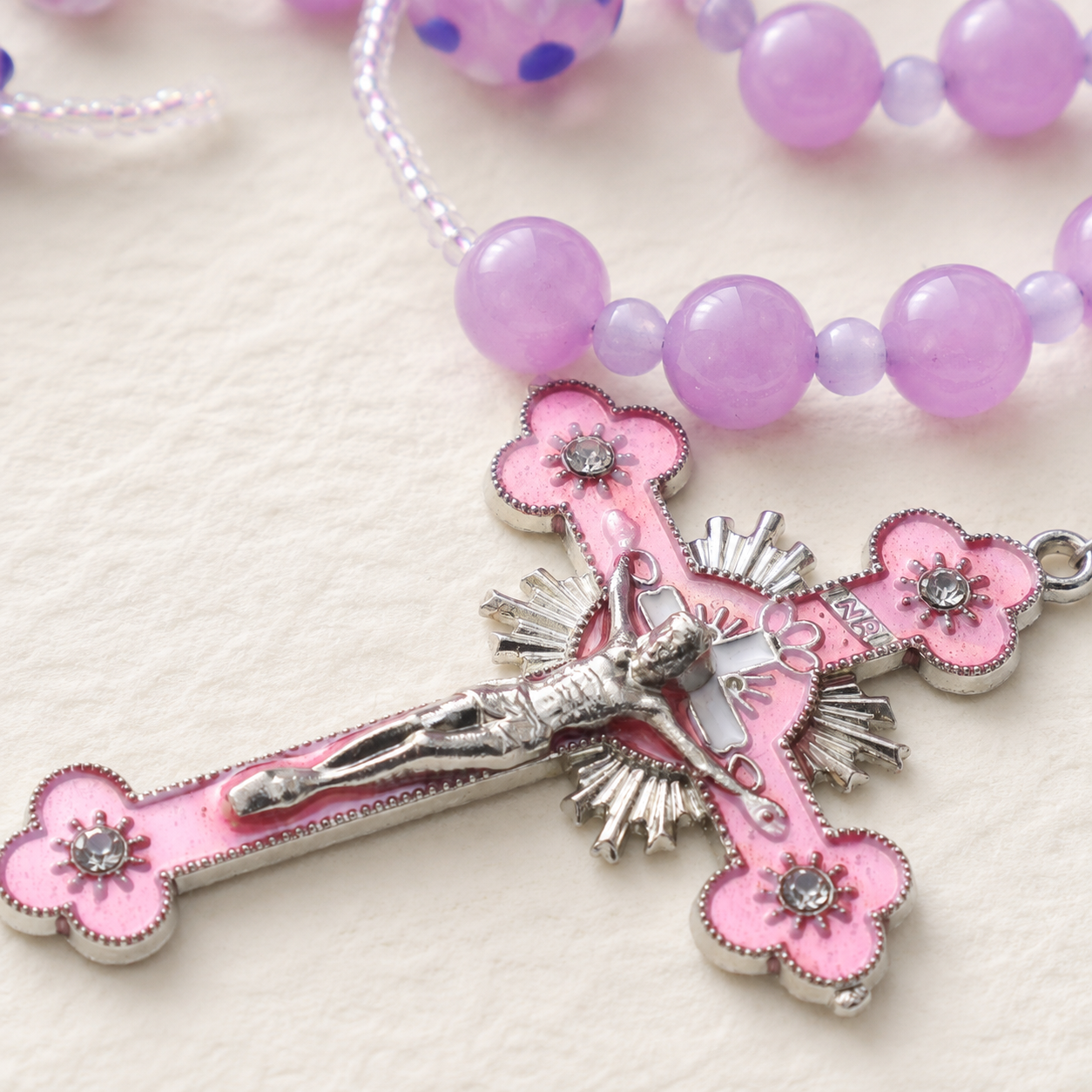 Pink crucifix pendant on a lavender Catholic rosary with floral bead accents and feminine faith design.