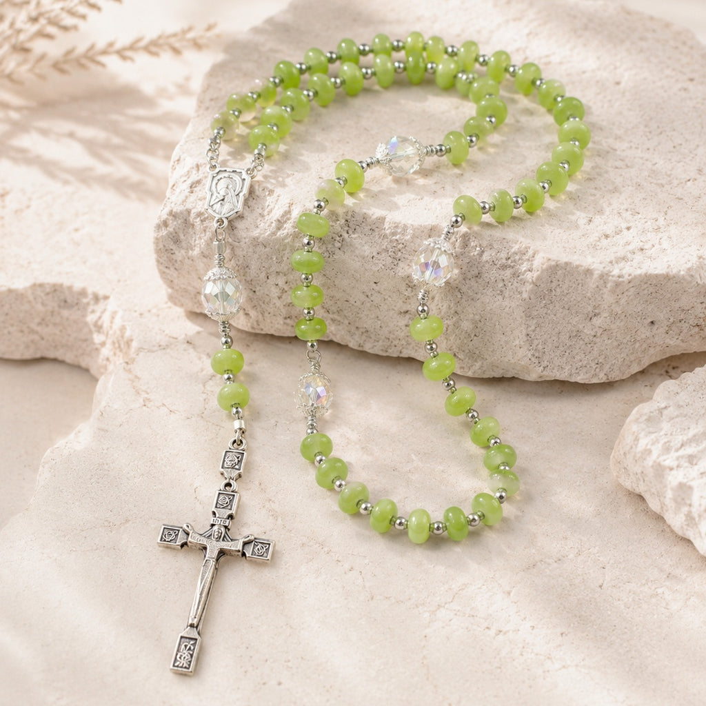 Green Catholic rosary with silver crucifix, Marian medal, and crystal accent beads displayed on a natural stone background