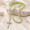 Green Catholic rosary with silver crucifix, Marian medal, and crystal accent beads displayed on a natural stone background