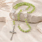Green Catholic rosary with silver crucifix, Marian medal, and crystal accent beads displayed on a natural stone background
