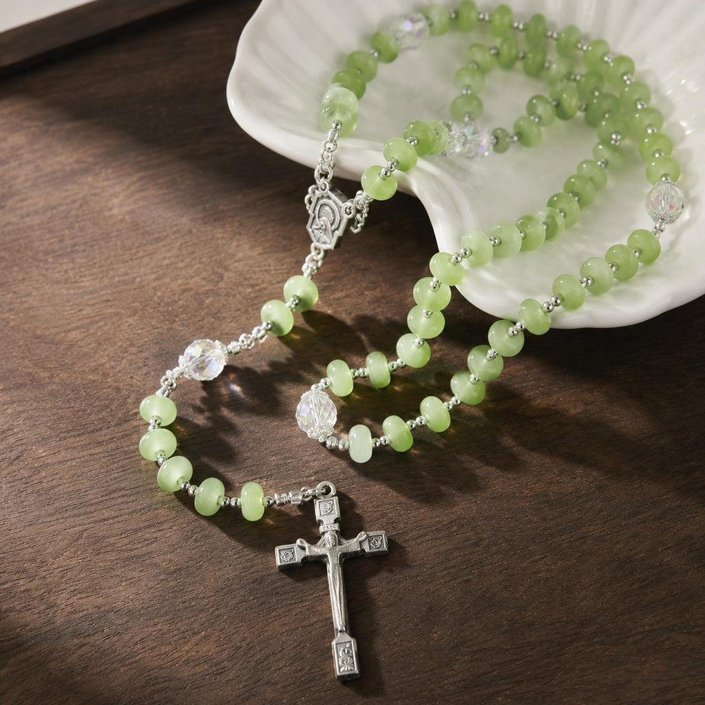 Soft green crystal-style rosary with silver cross, clear accent beads, and devotional Catholic medal on a light stone setting