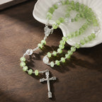 Soft green crystal-style rosary with silver cross, clear accent beads, and devotional Catholic medal on a light stone setting