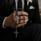 Black and gray Catholic groom rosary displayed with wedding ring, vow card, and silver crucifix as a meaningful marriage keepsake