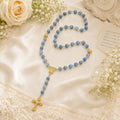 Something Blue wedding rosary hanging on a church pew with white ribbon and flowers, a Catholic bride gift for marriage blessing