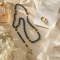 Deep blue Catholic wedding rosary with gold crucifix displayed on a bridal bouquet with soft pink and white flowers, designed as a meaningful bride prayer beads keepsake.