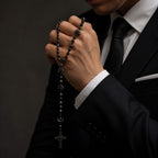 Black Catholic rosary for men with dark prayer beads and black crucifix, displayed on a soft ivory fabric background for a masculine religious keepsake.